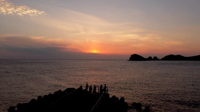 People on a jetty watching a beautiful sunset over the ocean