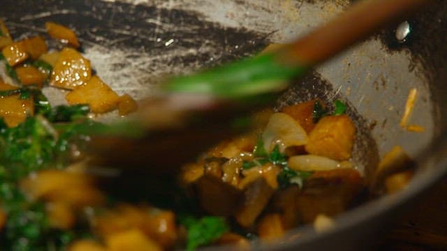 Sautéing spinach and tuna in a frying pan over an outdoor fire