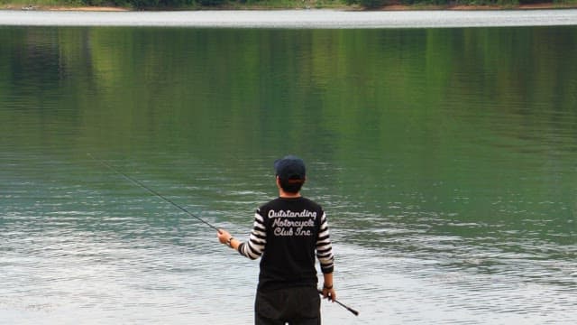 Person fishing by the serene lake on a cloudy day