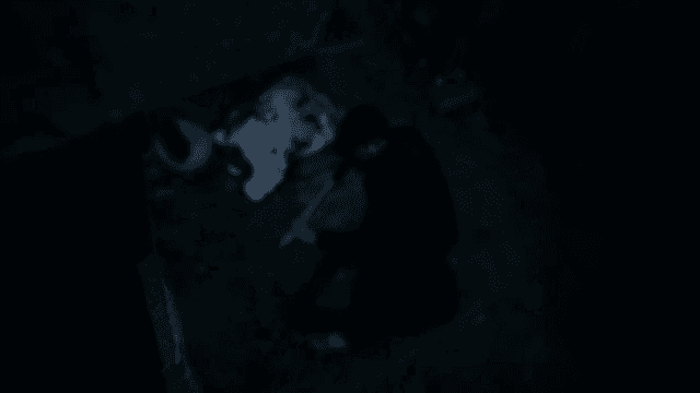 Person Digging Ground Beneath a Stone Wall at Night with Shovel