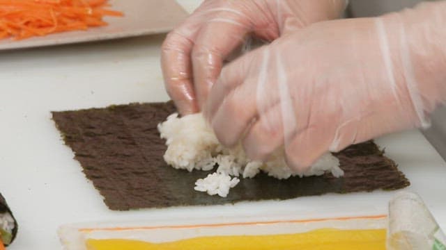 Preparing kimbap on a cutting board with hands wearing plastic gloves