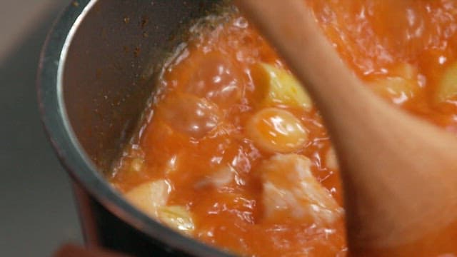 Cooking a bubbling tomato stew with wooden spoon