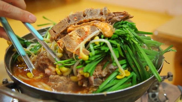 Tongs taking meat out of pork backbone stew with chives and bean sprouts