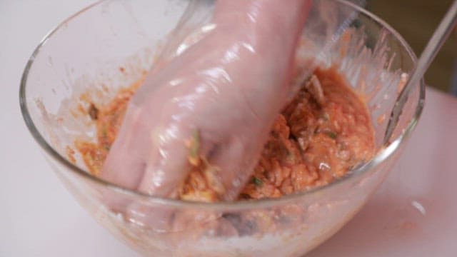 Mixing kimchi pancake batter in a glass bowl with hands wearing vinyl gloves