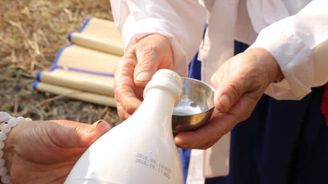 Elderly person preparing an outdoor traditional ritual with rice wine
