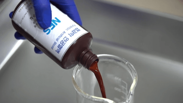 Gloved forensic scientist pours forensic artificial blood into a beaker