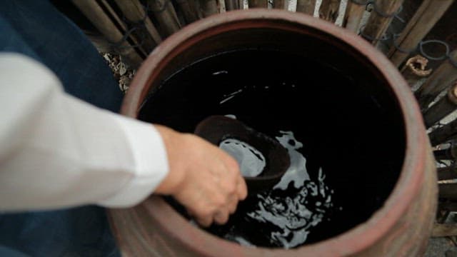 Soy sauce being poured into a ladle from a traditional Korean jar
