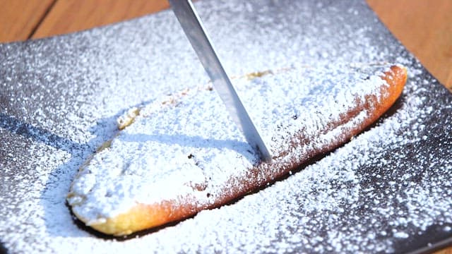 Cutting a sweet potato soufflé pancake sprinkled with powdered sugar with a knife