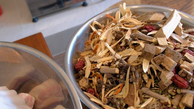 Various dried herbs and roots in a metal bowl