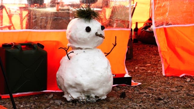 Snowman made with pin cones and pine branchses next to an orange tent