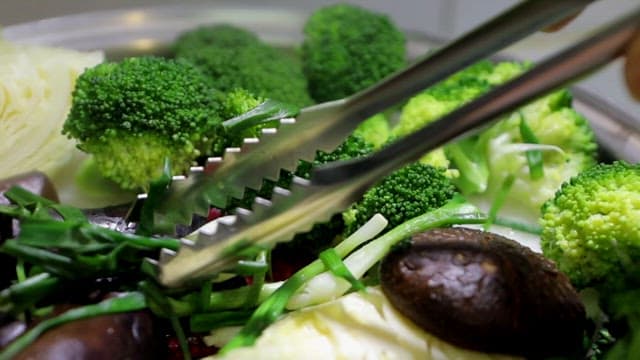 Various vegetables such as mushrooms, broccoli, and mushrooms being picked up with tongs