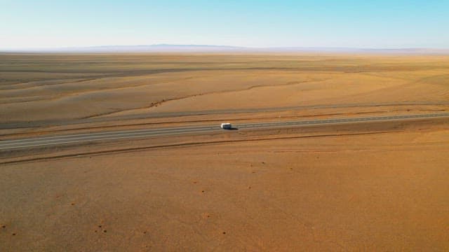 Lone Vehicle Traversing Vast Desert Highway