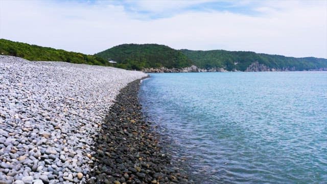 Pebble Beach with Lush Green Hills and Calm Sea