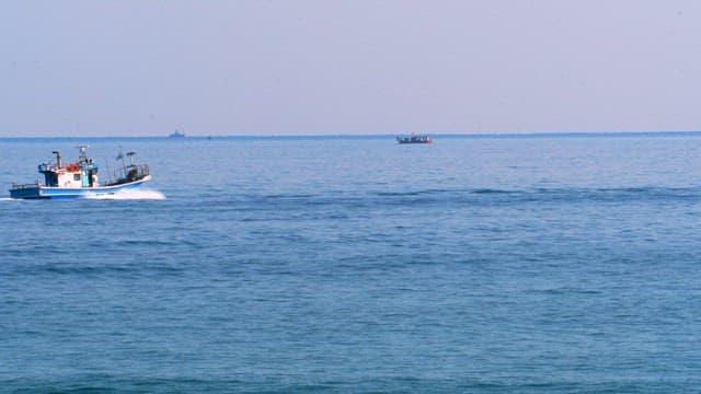 Fishing boat traveling across calm sea under clear sky