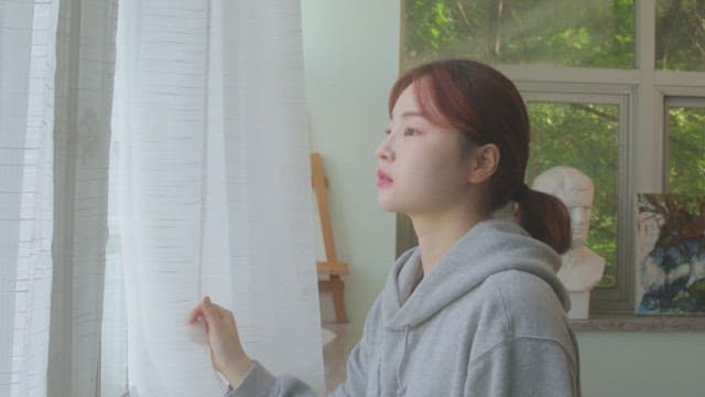 Student looking out the window in an art room with sculpture and painting