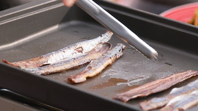 Grilling half-dried saury on a pan with tongs