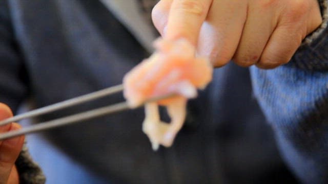 Person holding raw chicken piece with chopsticks