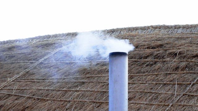 Smoke rising from a chimney on a thatched roof