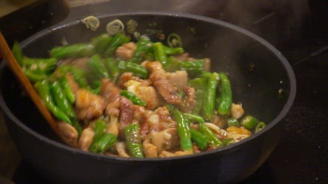 Cooking pork belly and peppers in a hot pan with wooden spoon