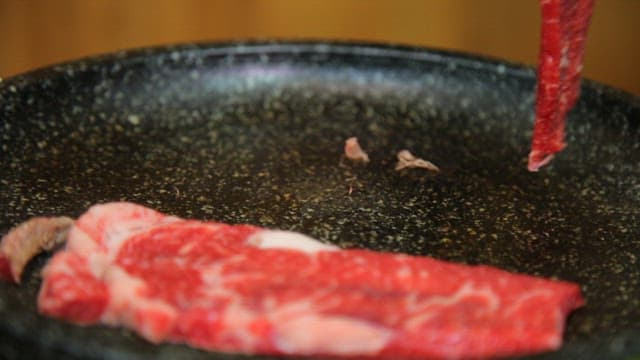 Raw beef being placed on a hot grill