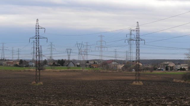 Rural field with multiple power line towers under a cloudy sky