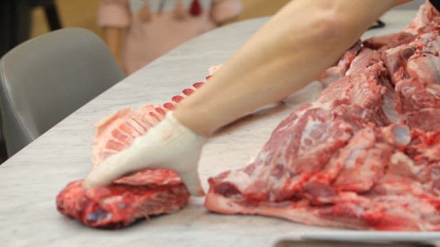 Person handling raw pork meat on a marble countertop
