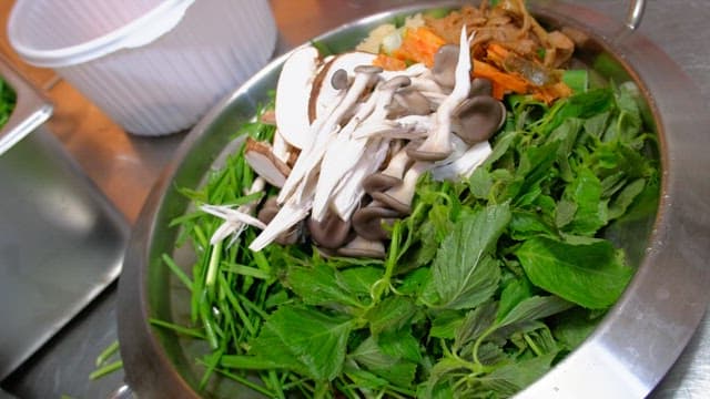Fresh greens and mushrooms in a metal bowl for hotpot dish