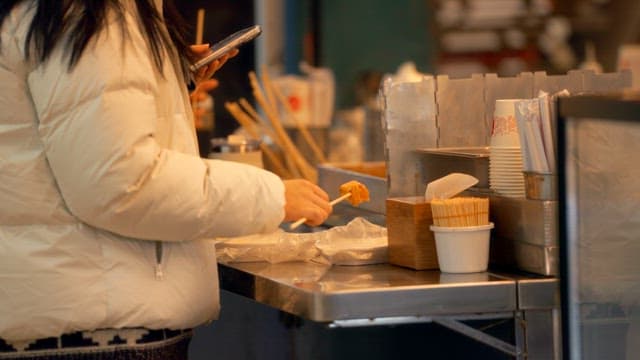 Person eating fish cake while using a smartphone at a street vendor