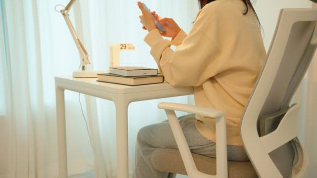 Woman using a smartphone at a desk in a calmly lit room
