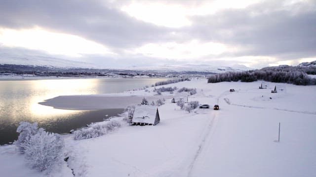 Snow-covered landscape with a lake and cabin