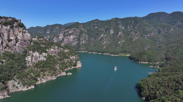 Tranquil Lake with a Boat Passing Between Lush and Majestic Mountains