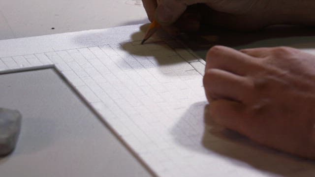 Grid pattern is drawn on a white piece of cardboard with a pencil
