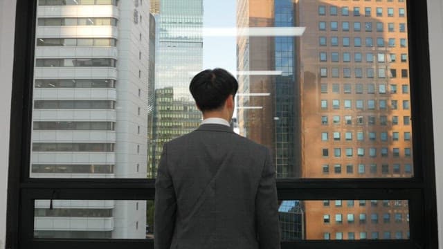 Man in a suit stretching while looking at the tall building outside his office window