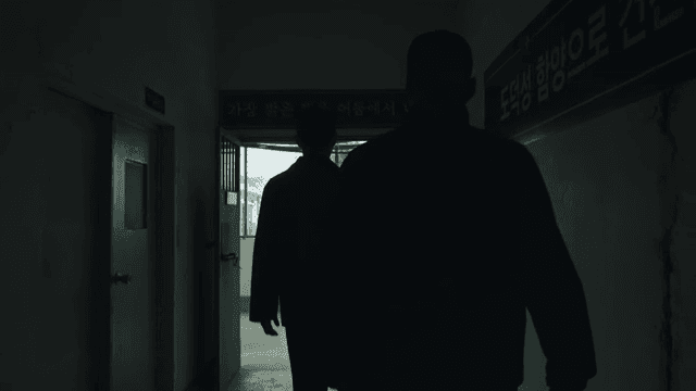Two men walking through a dark hallway in a prison