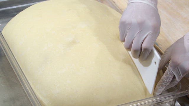 Taking a large piece of dough and placing it on a wooden cutting board