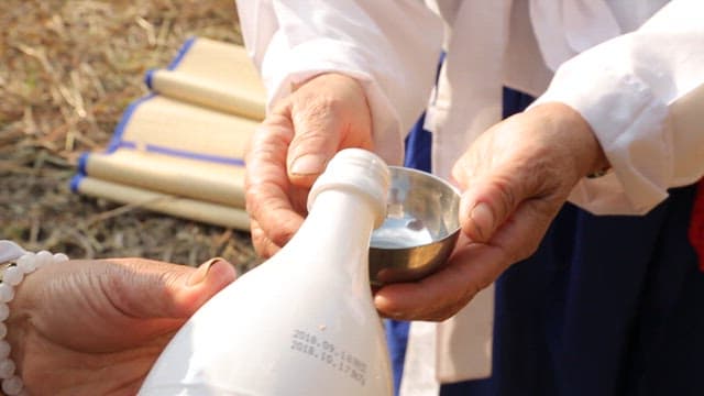Pouring makgeolli onto an outdoor ceremonial table