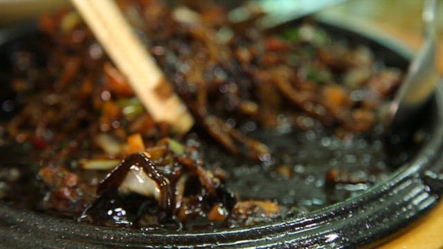 Chopstickful of seafood Jjajang noodles on an iron plate with steaming hot sauce