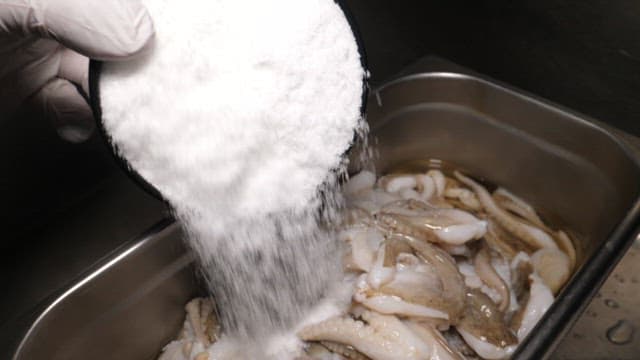 Hands in Gloves Preparing Seafood with Salt