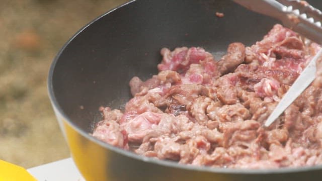 Cooking beef in a pan outdoors