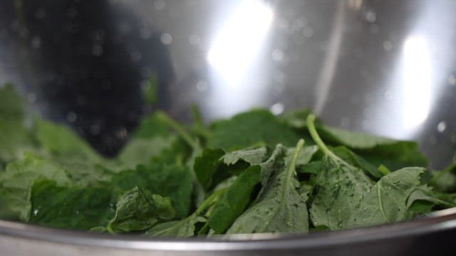 Fresh green leaves being washed and minced in a metal bowl