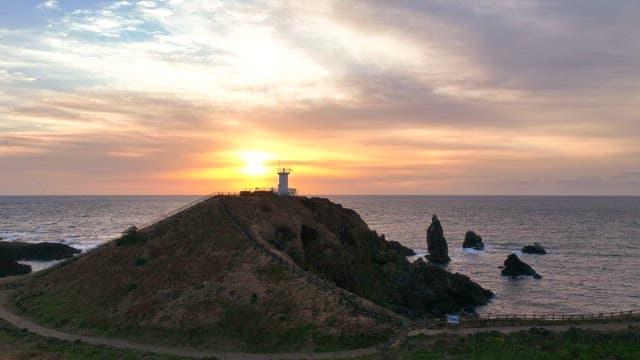 Lighthouse on a hill at sunset by the sea