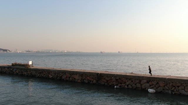 Person jogging on a breakwater with the peaceful sea at dusk