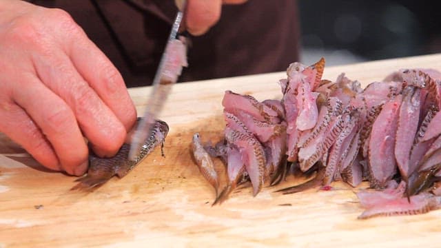 Slicing fresh damselfish on a wooden cutting board