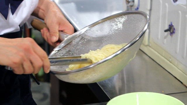 Noodles being strained and placed in a bowl