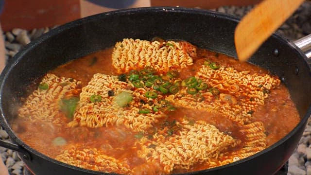 Boiling the ramen in a large pot with fresh green onions