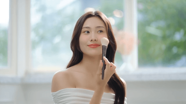 Woman applying makeup with a brush in a brightly lit room