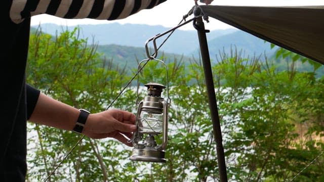 Person hanging camping lantern on a tent by the lakeside in the afternoon