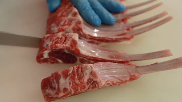 A chef in gloves precisely cutting rack of lamb in kitchen