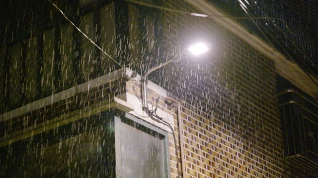 Nighttime rain pouring under a streetlight by a brick building