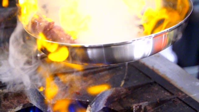 Flames rising from a pan with beef cooking